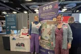 [Rosie and Erin stand next to a promotional banner for Make Your Mark that says "Help care for and celebrate Scotland's places and stories!".