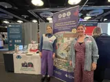 [Rosie and Erin stand next to a promotional banner for Make Your Mark that says "Help care for and celebrate Scotland's places and stories!".